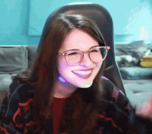 a woman wearing glasses is smiling while sitting in a gaming chair