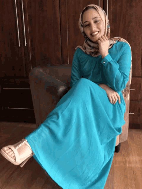 a woman in a blue dress sits on a chair with her legs crossed