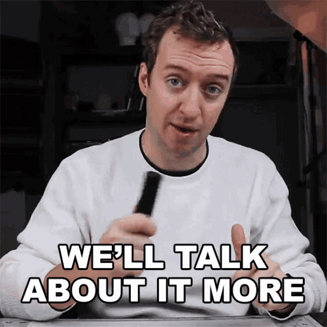 a man in a white sweater says " we 'll talk about it more " while holding a pen