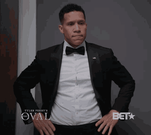 a man in a tuxedo is standing in front of a wall that says the oval