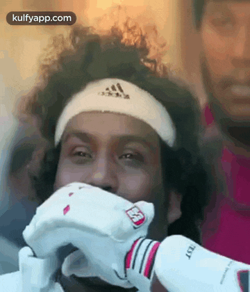 a man is wearing a headband and gloves and covering his mouth with his hand .
