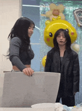 two women are standing next to each other with balloons in the background and one has a yellow balloon with a flower on it