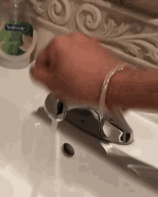 a person is washing their hands in a bathroom sink with a softsoap bottle nearby