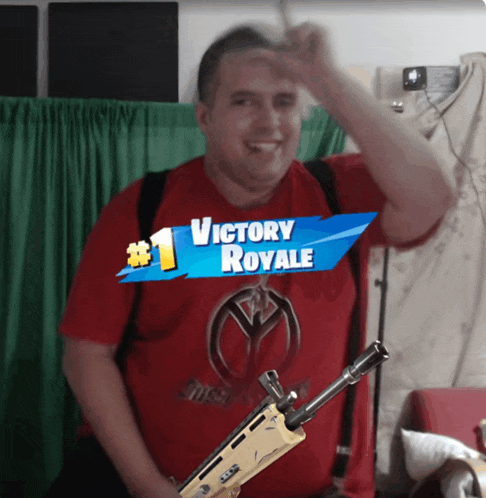 a man wearing a red shirt that says victory royale holds a gun