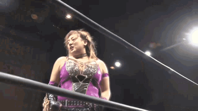 a woman in a purple tank top is standing in a wrestling ring with her arms outstretched