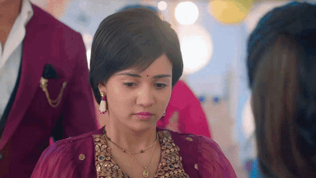 a woman in a purple top and gold necklace