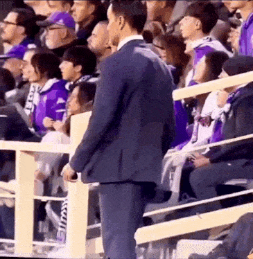 a man in a suit is standing in front of a crowd at a stadium .