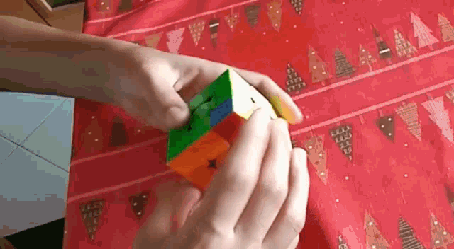 a person is playing with a rubik 's cube on a red table cloth with trees on it .