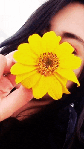 a woman is covering her face with a yellow flower