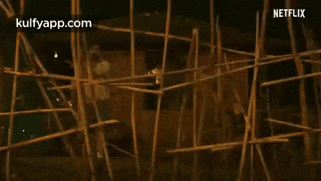 a man is standing in front of a building surrounded by a fence made of bamboo sticks .