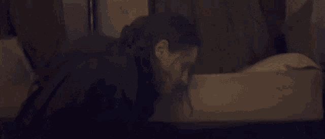 a person is laying on a bed with their head on a pillow in a dark room .