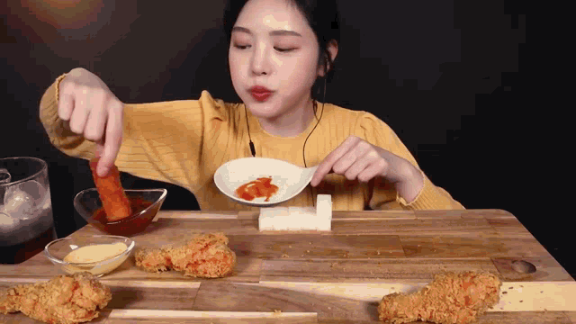 a woman in a yellow sweater is sitting at a table eating fried food