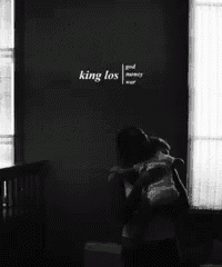 a black and white photo of two people hugging with the words king los written on the wall behind them