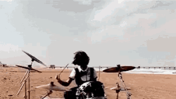 a person is playing drums on a beach with a blue sky in the background