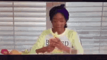 a woman in a yellow shirt is sitting at a table with a glass of water and a plate of food .