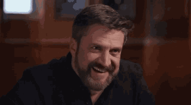 a man with a beard is smiling and making a funny face .