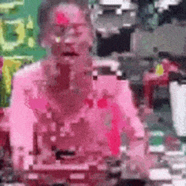 a woman with pink paint on her face is sitting at a table with a pink background .