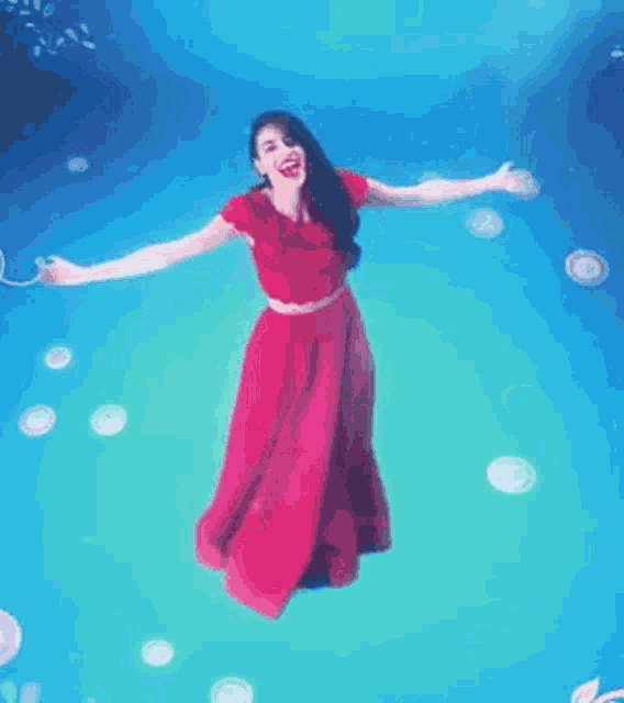 a woman in a red dress is floating underwater .
