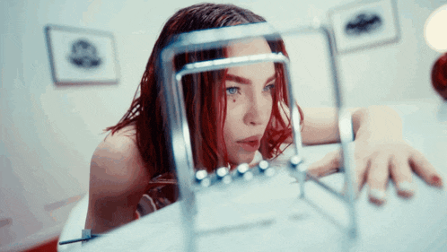 a woman with red hair looks at a newton 's cradle on a table