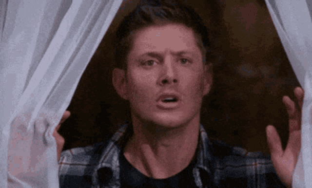 a man in a plaid shirt is looking out of a window with his hands outstretched .