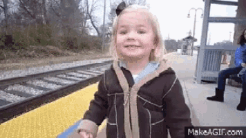 a little girl is standing in front of a train track and smiling .