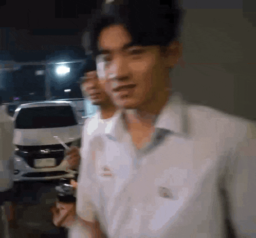 a man in a white shirt is standing in front of a white car at night .