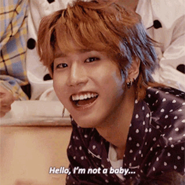 a young man in a polka dot shirt is smiling and says hello i 'm not a baby