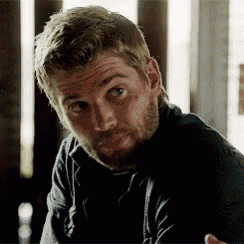 a man with a beard is sitting at a table with his arms crossed and looking at the camera .