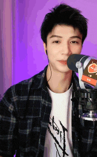 a man wearing headphones and a plaid shirt stands in front of a microphone ..