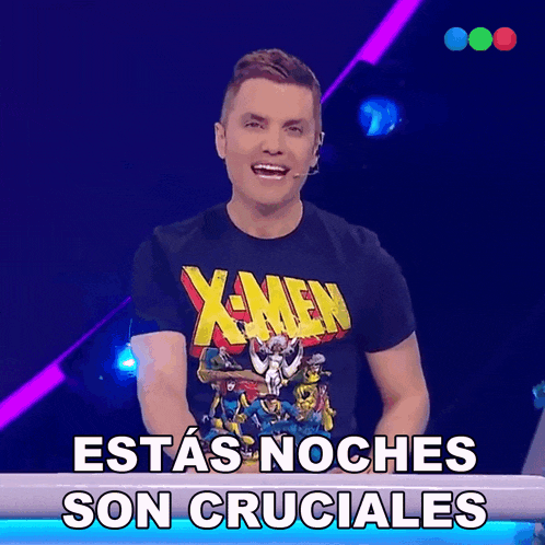 a man wearing a x-men shirt stands in front of a sign that says " estas noches son cruciales "