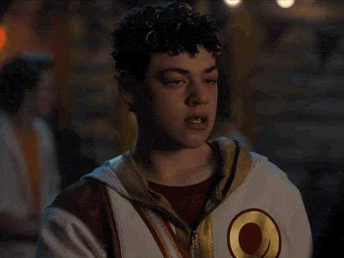a young man with curly hair is wearing a white jacket with a red circle on it