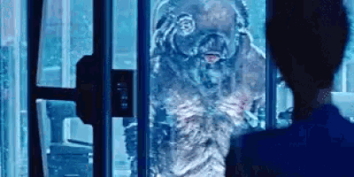 a woman in a blue shirt is looking at a monster in a glass cage .