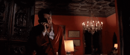 a man in a suit is talking on a cell phone in a room with a chandelier .