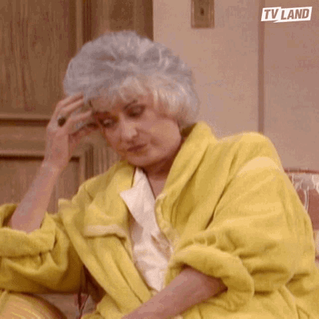a woman in a yellow robe is sitting on a couch with her hand on her head