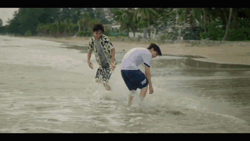two young men are running in the water on a beach .