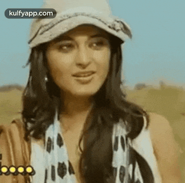 a woman wearing a hat and scarf is standing in a field and looking at the camera .