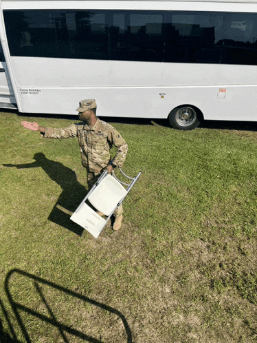 a man in a military uniform carrying a chair in front of a bus