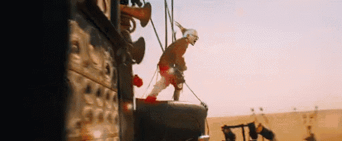 a man is standing on top of a large object in the desert holding a hammer .