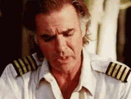 a man in a white shirt with gold stripes on the shoulder looks down .