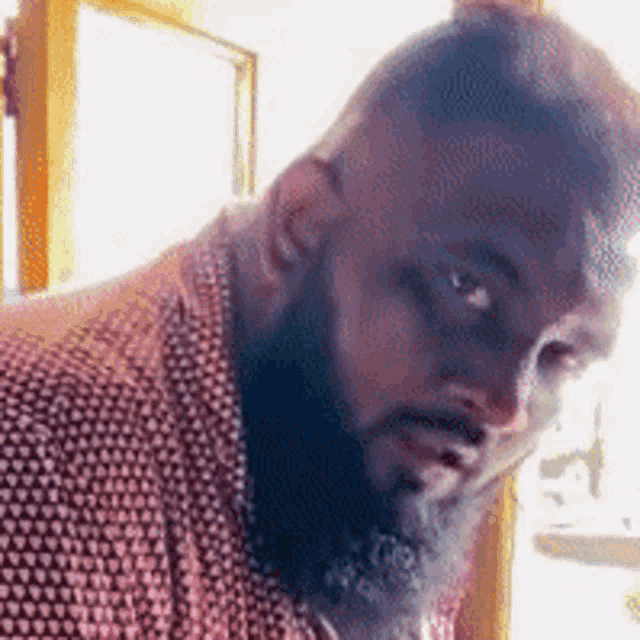 a man with a beard is looking at the camera while wearing a red and white shirt .