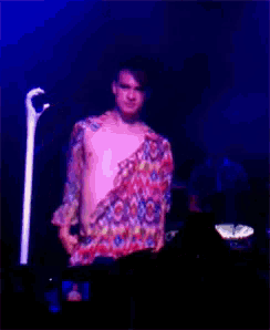 a shirtless man in a colorful shirt stands in front of a blue light