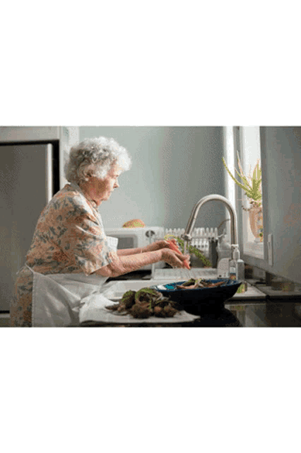 an elderly woman is washing vegetables in the kitchen sink