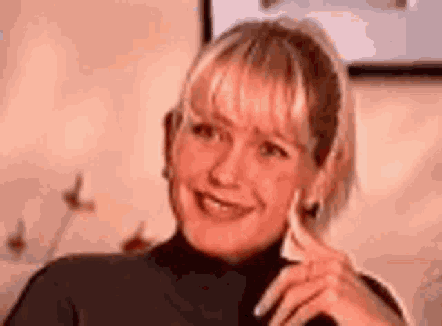 a woman in a black turtleneck is smiling and holding her hand to her ear .