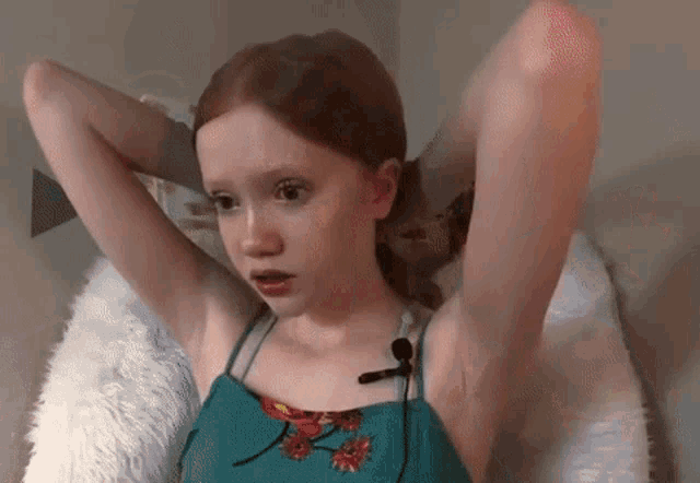 a young girl is sitting in a chair with her arms outstretched and a microphone attached to her ear .