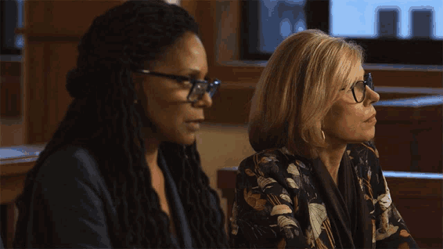 a woman wearing glasses sits next to another woman wearing dreadlocks