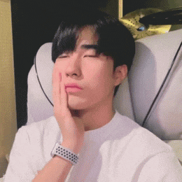 a man in a white shirt is sitting in a chair with his eyes closed and his hand on his face .
