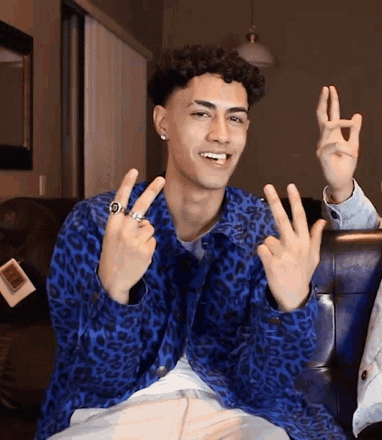 a young man wearing a blue leopard print jacket is making a peace sign with his fingers