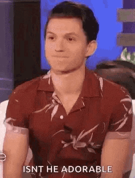 a young man in a red shirt is sitting on a couch and making a funny face .