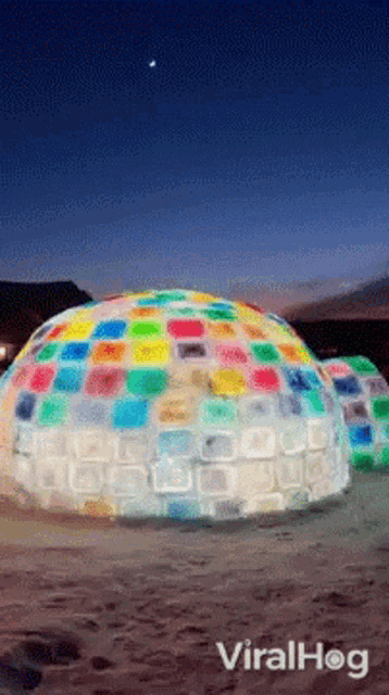 a colorful igloo made out of plastic bottles is on a sandy beach .