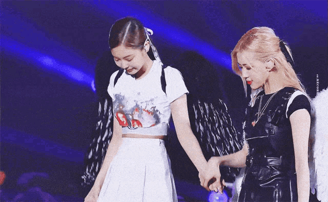 two girls with angel wings are holding hands on a stage with a purple background